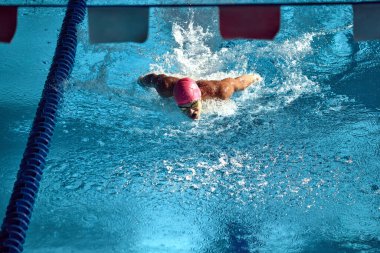 Competitive swimmer, wearing pink swim cap and goggles, powers through water with butterfly stroke, creating dynamic splash in blue swimming pool lane. Concept of aquatic sport, energy. clipart