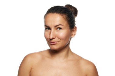Makyajsız güzel bir kadının portresi, çıplak omuzlarıyla poz veriyor, beyaz stüdyo arka planında kameraya gülümsüyor. Yüz bakımı, kaldırma, spa prosedürleri, ameliyat kavramı.