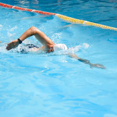 Genç bir adamın dinamik görüntüsü, hareketli bir yüzücü, güneşli bir günde havuzda serbest yüzme vuruşu. Profesyonel spor, rekabet, aktif ve sağlıklı yaşam tarzı kavramı. Ad