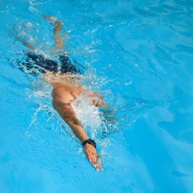 Genç bir adamın dinamik görüntüsü, hareketli bir yüzücü, güneşli bir günde havuzda serbest yüzme vuruşu. Profesyonel spor, rekabet, aktif ve sağlıklı yaşam tarzı kavramı. Ad
