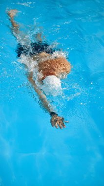 Kaslı adamın üst görüntüsü, hareket halindeki beyaz şapkalı yüzücü, antrenman sırasında havuzda yüzme gücünü gösteriyor. Profesyonel spor, rekabet, aktif ve sağlıklı yaşam tarzı kavramı.