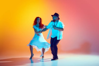 Salsa antrenmanına odaklanmış, dans eden çiftler, neon ışığı altında eğilim turuncu arka plana karşı hassasiyet ve akıcılık üzerine çalışırlar. Dansın romantik havası. Dans konsepti, performans.