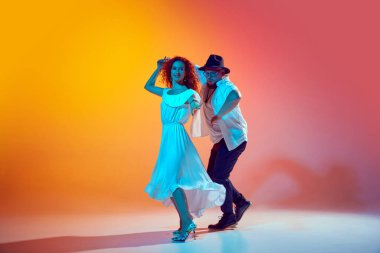 Salsa dansçıları, güçlü bir şekilde prova yapan çiftler, tekniklerini geliştiren, gradyan turuncu arka plana karşı neon ışığında adımlarını atan çiftler. Dansın romantik havası. Performans, sanat, eğlence anlayışı.