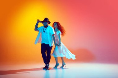 Neşeli Latin dansçılar yoğun bir şekilde prova yaparak, salsa danslarını ve ritmlerini neon ışığında turuncu arka plana karşı mükemmelleştiriyorlar. Dans, performans, sanat, eğlence anlayışı. Ad