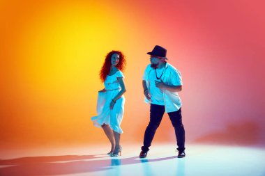 Salsa ikilisi enerji ile prova yapar, akışkan hareketlere ve neon ışığındaki ritmik hassasiyete eğimli turuncu arka plana odaklanır. Dansın romantik havası. Performans, sanat, eğlence anlayışı