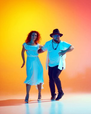 Birkaç dansçı enerjiyle prova yapıyor, akışkan hareketlere ve neon ışıkta eğimli turuncu arka plana karşı ritmik hassasiyete odaklanıyor. Dans, performans, sanat, eğlence kavramı.