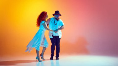 Enerjik salsa antrenmanlarına katılan dansçılar, hareketli turuncu arka plana karşı neon ışığı altında adımları ve ritmi mükemmelleştirmeye çalışıyorlar. Dans, performans, sanat, eğlence kavramı.