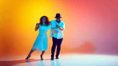 Latin dansının ruhu. Salsa 'nın canlı adımlarını pratik yaparak, ikili, neon ışıkta rengarenk turuncu arka plana karşı yeteneklerini keskinleştiriyor. Dansın romantik havası. Dans, performans, sanat kavramı