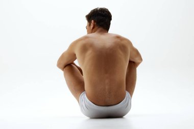 Beyaz donlu, formda bir gencin arka planda çekilmiş fotoğrafı zeminde oturuyor. Omurgası beyaz arka planda. Vücut bakımı, erkek sağlığı, doğal güzellik, gençlik, erkeklik kavramı. Ad