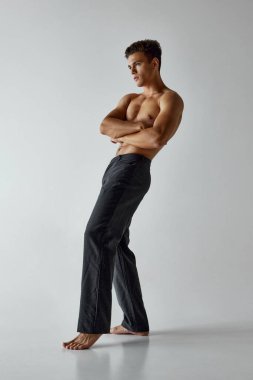 Pantolonsuz poz veren genç kaslı adam ellerini göğsüne koydu ve gri stüdyo geçmişine karşı güvenini gösterdi. Vücut bakımı, erkek sağlığı, doğal güzellik, erkeklik kavramı. Ad