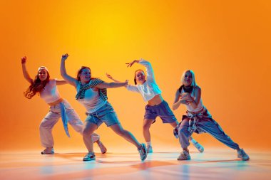 Bir grup enerjik dansçı, gündelik retro kıyafetleriyle, parlak neon ışıklarıyla, gradyan stüdyo arka planına karşı çağdaş dans ediyorlar. Müzik, moda ve sanat kavramı, hareket, spor ve hobi.