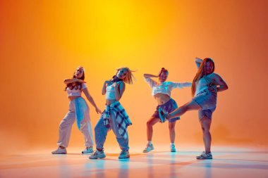 Dörtlü genç kızlar, gündelik giyinen dansçılar hareketli neon ışıkta, gradyan stüdyo arkaplanına karşı cesur pozlar veriyorlar. Müzik, moda ve sanat kavramı, retro ve modernite, hareket, hobi.