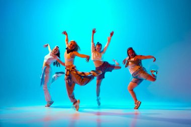 Sanatçı kızlar, sokak kıyafetleri içindeki dansçılar parlak mavi arka plana karşı cesur pozlar verirler, kendine güven ve yaratıcılık yayarlar. Müzik, moda ve sanat kavramı, modernlik, hareket, hobi. Ad