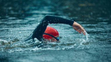 Kırmızı şapkalı bir triatloncu açık denizde trenlere odaklanır. Aerodinamik biçimi ve triatlon yüzme eğitimine olan bağlılığını yansıtır. Spor müsabakası, antrenman, eğlence anlayışı