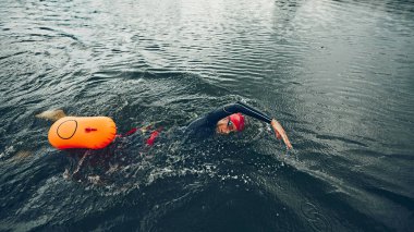 Yüzücülerin siyah dalış kıyafetleri ve kırmızı şapkalı sudaki gücü, her vuruş kusursuz, triatlona hazırlanıyor. Spor müsabakası, spor, eğlence, sağlıklı yaşam tarzı kavramı.
