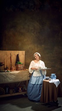 Genç tombul kadın, bakire, tarihi elbise tepsisi içinde, eski mutfak eşyaları ve otlarla çevrili garson olarak. Bar, bar, Bavyera tarzı, Ekim festivali kavramı. Dönem karşılaştırmaları.