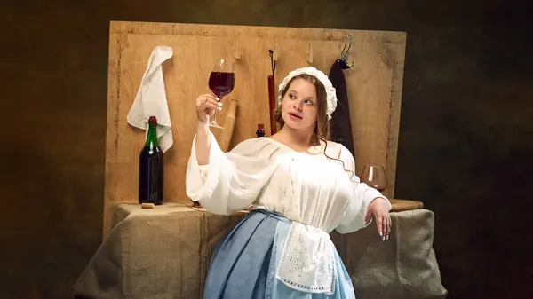 stock image Young chubby medieval woman in vintage clothes holding glass of wine standing at ancient bar counter and enjoy evening. Concept of bar, pub, Bavarian style, Oktoberfest. Comparisons of eras.