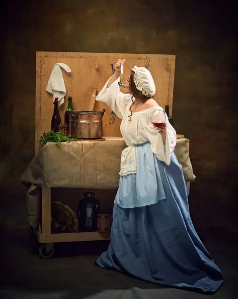 stock image Woman in traditional attire taste-tests ladle of beer, holding glass in one hand, amidst rustic kitchen with vintage cookware and ingredients. Concept of bar, pub, Bavarian style, Oktoberfest. Ad