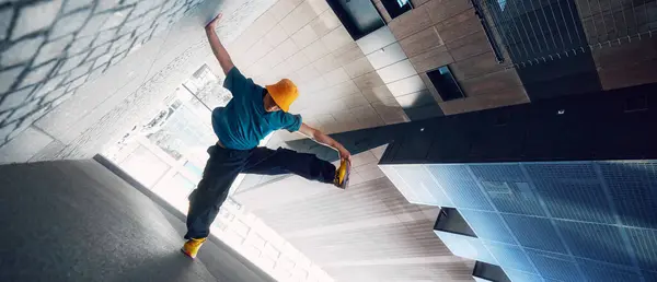 stock image Creative photo. Dancer in yellow bucket hat and blue shirt performs handstand against modern urban backdrop. Strength and style. Concept of lifestyle, extreme sport, freestyle, activity, motion. Ad