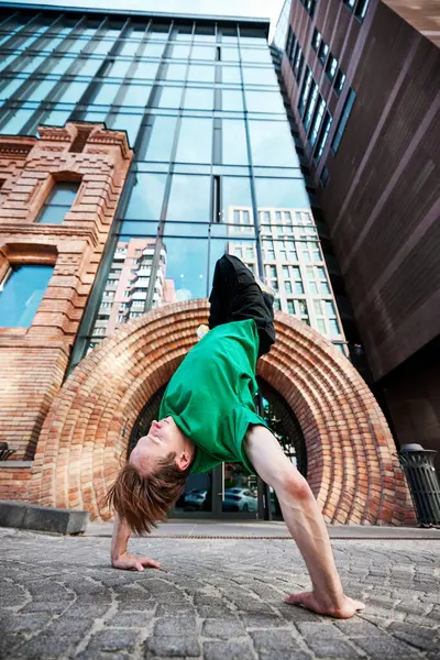 Stock image Mid-flip breakdancer, posing standing on hands against the backdrop of tall, modern buildings, showcasing urban agility. Concept of lifestyle, extreme sport, freestyle, activity, motion. Ad