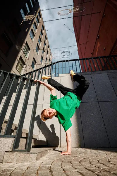 stock image Young athletic man, fashionista in colorful attire, performs powerful handstand flip against city backdrop. Modern architecture. Concept of lifestyle, extreme sport, freestyle, activity, motion. Ad