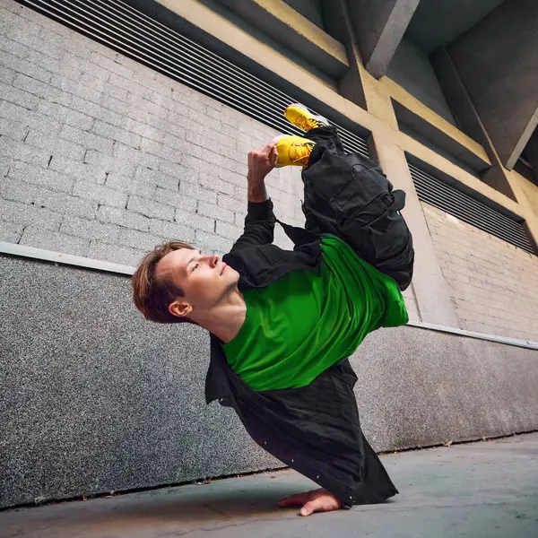 stock image Breakdancer in action, flipping upside down in front of tall urban buildings, his yellow shoes adding pop of color to dynamic scene. Concept of lifestyle, extreme sport, freestyle, activity, motion.