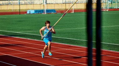 Motive olmuş sırıkla atlamacı, kaslı mavi spor giysili genç adam direkle hareket halinde, hassas ve güçlü bir şekilde çalışıyor. Spor, rekabet, turnuva, aktif yaşam tarzı, güç konsepti