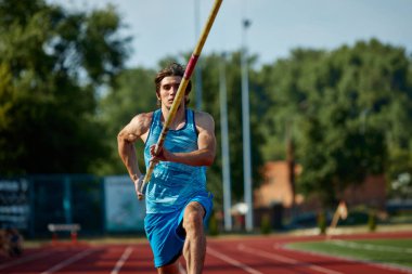 Açık stadyum pistinde atlet eğitimi, yeni yükseklikler hedefleyen, direkle koşan, yeteneklerini gösteren odaklanmış bir adam. Spor, rekabet, turnuva, aktif yaşam tarzı, güç kavramı