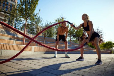 Atletik çift, kadın ve erkek dinamik antrenman yapıyor, savaş halatlarıyla antrenman yapıyor, güç, dayanıklılık ve güç gösteriyor. Spor anlayışı, aktif ve sağlıklı yaşam tarzı, fitness