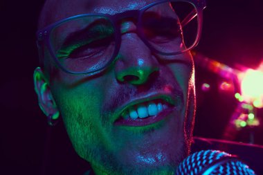 Canlı ışıklar şarkıcıların yüzünü aydınlatır, açık ağzı ve yoğun ifadesi canlı performansın ham enerjisini yakalar. Müzik ve parti kavramı, hobi ve iş, enerji, müzik festivalleri. Ad