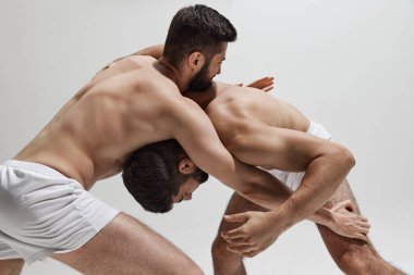 İki rakip, eşit derecede uyumlu, güç ve irade testi için güreşiyor, ikisi de sıcak gri arka planda birbirlerini alt etmeye çalışıyorlar. Erkek sağlığı, güzellik ve moda, fitness kavramı. Ad.