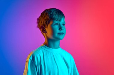 Küçük bir çocuğun portresi, mavi-pembe renkli bir stüdyonun arka planına karşı neon ışıkta mesafeye güvenle bakar. Çocuk kavramı, insani duygular, moda ve tarz, yaşam tarzı. Ad
