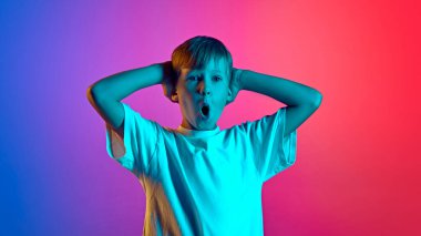 Şaşırmış, duygusal küçük bir çocuk neon ışığın altında el ele tutuşuyor. Gradyan mavi-pembe stüdyo arka planına karşı. Çocuk kavramı, insani duygular, moda ve tarz, yaşam tarzı. Ad