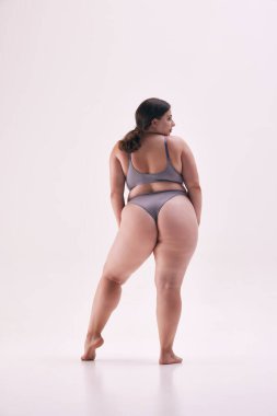 Güzel, genç bir bayanın arka plan fotoğrafı, model boyutu artı gri iç çamaşırlarıyla poz vermek beyaz stüdyo arka planına karşı güven yayıyor. Doğal güzellik kavramı, vücut pozitifliği, kendini sevme. Ad
