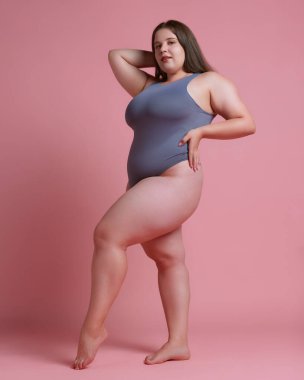 Çekici bir kadının tam vücut fotoğrafı, artı pembe stüdyo arka planında gri mayo giymiş bir model. Doğal güzellik kavramı, vücut pozitifliği, kendini sevme, kaplıca tedavisi. Ad