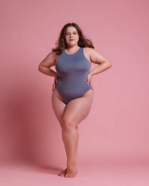 Kendine güvenen, iri yarı, gösterişli bir kadın, elleri kalçasında, pembe stüdyo geçmişine karşı doğal güzelliğini kucaklıyor. Vücut pozitifliği, kendini sevme, spa tedavisi, moda kavramı. Ad