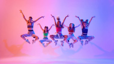 Artistik ve sportif genç kızların neon ışıkta gradyan pembe arka plana karşı performans sergiledikleri enerjik bir fotoğraf. Spor ve hobi kavramı, çocukluk, arkadaşlık, hareket. Dans okulu.