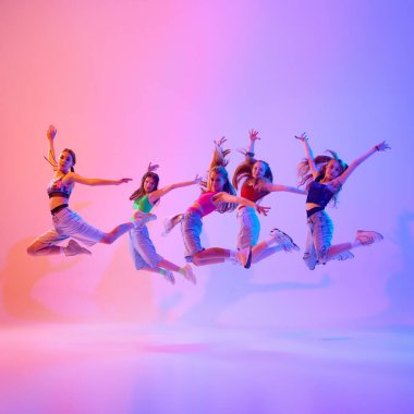 Genç kızların dinamik fotoğrafı, gençlerin performansı, neon ışıklarıyla havada zıplaması, gradyan pembe arka plan. Spor ve hobi kavramı, çocukluk, arkadaşlık, hareket. Dans okulu.