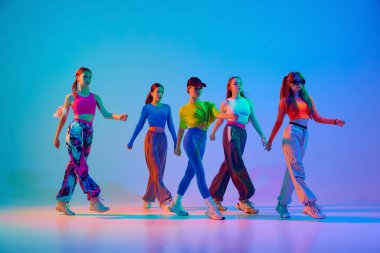 Zarif kızlar, hareketli dans eden düşünceli şık renkli kıyafetler içinde neon ışıklarıyla gradyan stüdyo arka planına karşı dans ediyorlar. Spor ve hobi kavramı, çocukluk, arkadaşlık, hareket. Dans dersleri..