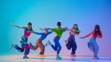 Şık giyimli, spor kıyafetleri olan genç kızlar, stüdyonun arka planına karşı neon ışıkta hip-hop yapıyorlar. Senkronize. Spor ve hobi kavramı, çocukluk, arkadaşlık, hareket. Dans dersleri..