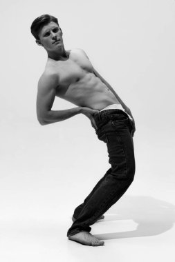 Siyah ve beyaz bir adam fotoğrafı, arkaya doğru eğiliyor, beyaz stüdyo arka planına karşı kotuyla dramatik bir poz veriyor. Erkek sağlığı kavramı, doğal güzellik insanları, moda, kişisel bakım.