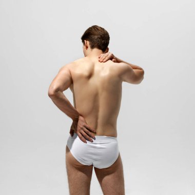 İnsanın bir elinin belinde, diğerinin boynunda durduğu arka plan beyaz arka planda gerginlik veya yorgunluk hissi uyandırıyor. Erkek sağlığı kavramı, doğal güzellik insanları, moda.