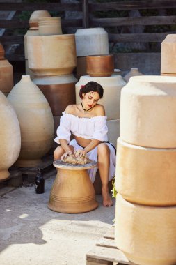 Klasik güzelliğe sahip genç bir kadın, dışarıdaki çömlek atölyesinde büyük kavanozlarla dolu bir kil işçiliğine dalmış. Yaz sonu kavramı, hasat, seyahat, doğal güzellik, kültür.