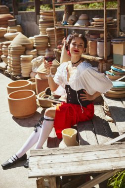 Neşeli bir ifadeyle, kadın bardağıyla poz veriyor, kutlamanın ve eğlencenin özünü yakalıyor. Yaz sonu kavramı, hasat, seyahat, doğal güzellik, kültür.