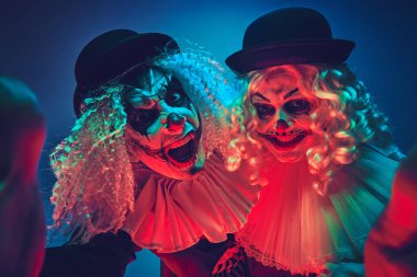 Ürkütücü palyaço çiftin portresi neon ışıkta arka plana bakıp şakacı bir poz veriyor. Mutlu Cadılar Bayramı konsepti, parti, şenlik havası, kutlama. Ad