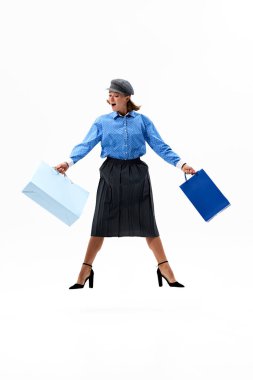 Mavi ve siyah kıyafetler giymiş, alışveriş torbalarıyla atlayan başarılı alışveriş çılgınlığından sonra neşesini ve enerjisini sergileyen bir kadın. Alışveriş kavramı, Kara Cuma, moda ve tarz, satış.