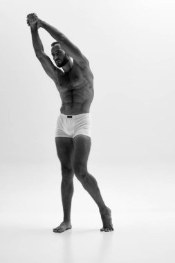 Erkeğin yan profilinin dinamik görüntüsü, kolu gerilmiş ve kasları kasılmış. Yoğun bakışlar ve yontulmuş vücut. Siyah beyaz fotoğraf. Güzellik ve moda kavramı, tarz ve gençlik, erkek sağlığı.