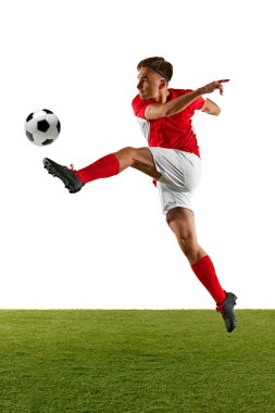 Kırmızı ve beyazlı odaklanmış futbolcu, antrenman sırasında hızlı tekme atıyor. Sporcu, beyaz stüdyo geçmişine karşı yeşil sahada iş başında. Şampiyonluk konsepti, spor müsabakaları, final maçı. Ad
