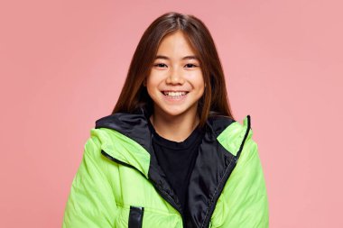 Genç esmer kız, kameraya gülümseyen öğrenci pastel pembe arka plana bakıyor. Kış gündelik tarzı. İnsan duyguları kavramı, okul, kış tarzı. Ad