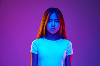 Stüdyonun arka planında, neon ışıkta sakince kameraya bakan genç bir kızın portresi. Belirli bir ifade. İnsani duygular, okul, güzellik ve tarz kavramı. Ad